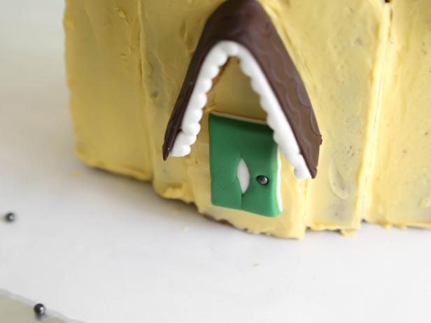 Use green and white fondant to create the home's front door. Press on a dragree as the &quot;doorknob&quot;.