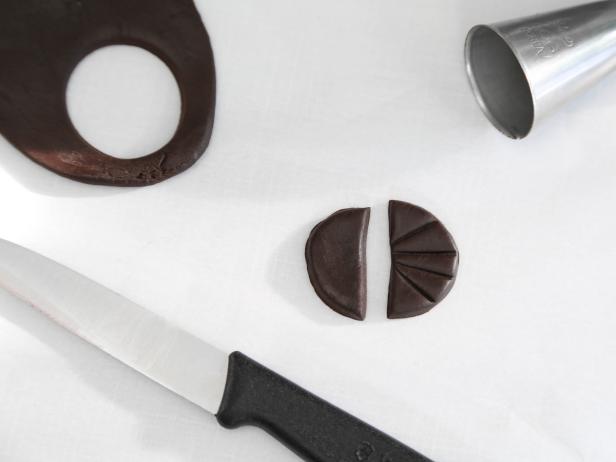Cut a 1 1/4-inch-diameter circle of chocolate fondant rolled to 1/4-inch thickness using a large end of a piping tip or a bottle cap. Cut in half and press lines radiating from the center with the back of a knife.