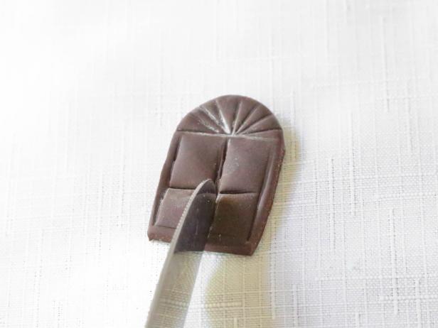 Cut a small arched window, about 3/4 x 1 1/2 inches from a piece of chocolate fondant rolled to 1/4-inch thickness. Create crisscross windowpane impressions with the back of a knife. Adhere piece to the right of the door using royal icing.