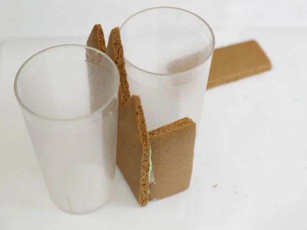 In step 9 of this project, attach a side gingerbread piece on either side, butting the short ends against the candy-coated short ends of the front gingerbread piece. Hold the pieces in place for 2-3 minutes, or use a tall tumbler as a prop.