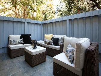 Gray Fenced-In Patio With Tile Floor and Brown Rattan Furniture