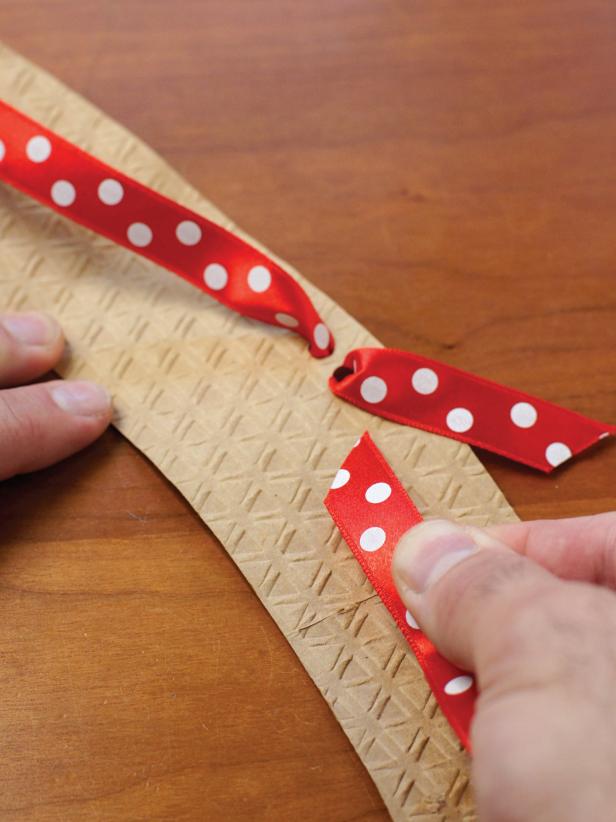 1. Carefully undo the cardboard sleeve where it is glued. Turn over.2. Punch two holes about 1/4-inch apart at the top/middle of the sleeve.3. Thread a ribbon through one hole from the front and through the other hole from the back (Image 1).4. Repeat for the other side with the other end of the ribbon.5. Attach a small ornament (if desired) and tie a bow with the ribbon (Image 2)