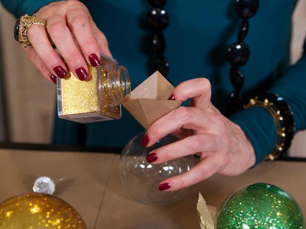 Designer Robin Baron pours glitter through a funnel into glass Christmas bulbs to create custom ornaments in any color scheme.