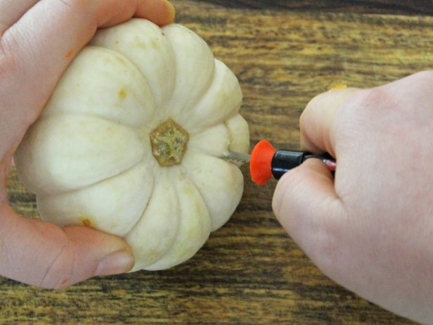 For the first step, use a pumpkin saw to cut a circle around the top of the white pumpkin.