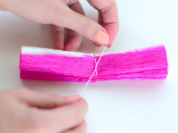 Cut a piece of thread and tie it tightly around the folded crepe paper, sliding it into the cut slit at the center.