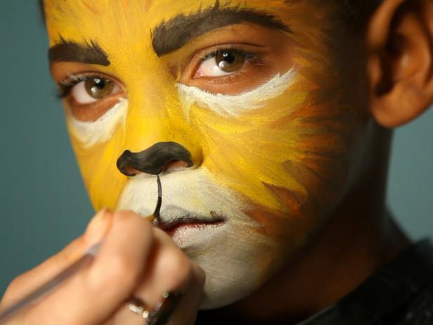 To give your child a ferocious lion’s face for Halloween, simply paint a basic orange and yellow face. Darken and thicken eyebrows with black or dark brown paint or shadow. Dip a thin paintbrush into water then coat with a generous amount of black paint. Paint nose black, focusing on the bottom tip. Next, paint a line connecting the bottom of the nose to the top lip, creating a cat-like mouth separation.