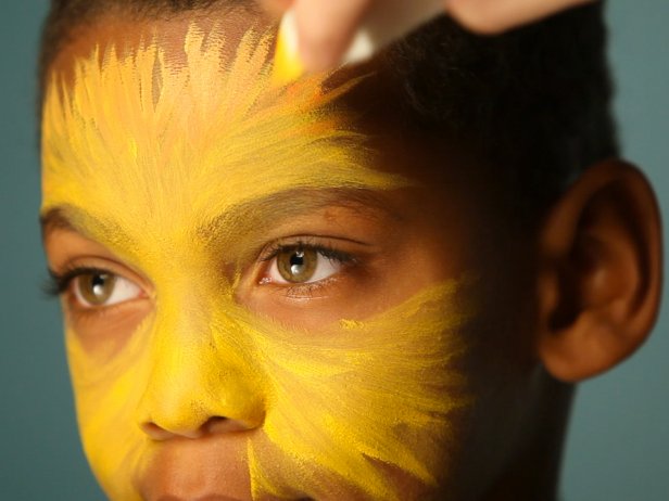 To create a base for your lion makeup, begin by dampening a sponge then picking up some of the yellow face paint. Tip: When using dry face paints, be sure to get sponge or brush wet before dipping into paint. Have child close their eyes, then apply yellow paint to the center of their face and blend out. Using the same sponge, add orange to the yellow paint's edges and blend out further to create a blended ombre effect. Apply orange paint like brushstrokes to resemble fur.