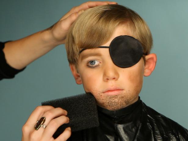 To create pirate makeup, darken the child’s eyebrows with eye shadow. Add an eye patch to one eye, and add brown shadow under the uncovered eye to mimic dark circles. Dip a stippling sponge in wet brown eye shadow or face paint, and then dab onto the chin and above the lip to give your pirate an unshaven look. Another option is to leave the top lip bare of makeup and adhere a fake mustache using eyelash glue, spirit gum or liquid latex. Tip: Be sure to test for any allergies before using any of these products, and have the proper remover on hand. Also, be sure to read all the information on product labels. Put together a costume of ripped clothing and add accessories like a bandana, a pirate hat, gold coins, a clip-on earring, hook or stuffed parrot — let your creativity run wild to give your pirate a unique look.