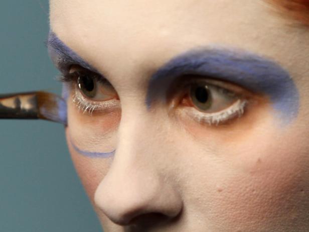 Using a brush, dip into a pot of cream-based makeup color in a sky-blue shade. Create large circles surrounding the eyes starting at the eyebrows and continuing all the way around. Fill in the top half of the circle, covering eyelids, and begin to fill in the bottom as well — avoiding the area where you put the white eyeliner.