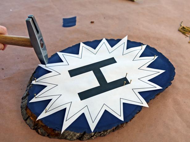 Center template onto plaque. Keep paper taut and start hammering nails into alternating points of the starburst. Continue adding nails approximately half an inch apart all around the outer edges of the starburst and letter.