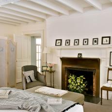 White Country Bedroom With Fireplace and Exposed Beams