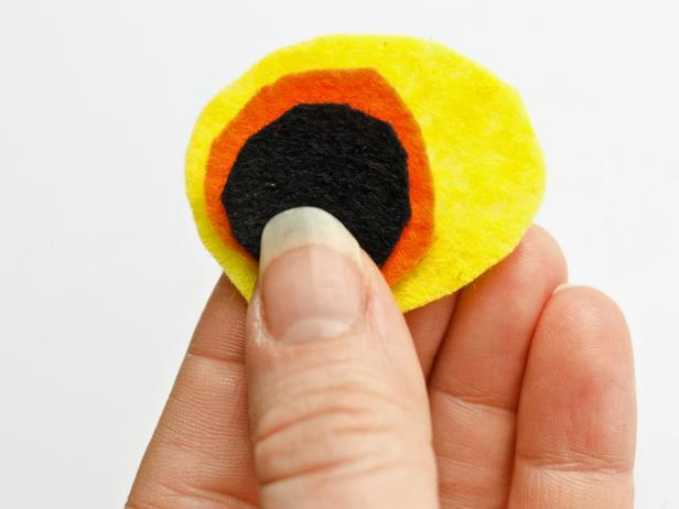 Layer yellow, orange, and black felt cutouts to create two eyes for the dinosaur costume. Pin one on each side of hood.