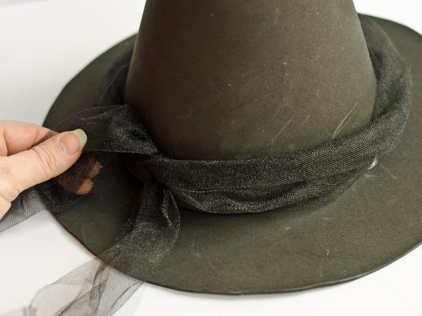 To embellish the witch's hat, tie a reserved piece of tulle around it. Secure the tulle with a simple knot in the back, held in place with a dab of hot glue.