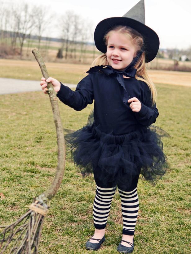 Small child wearing a homemade witch's costume, with a twig broom.