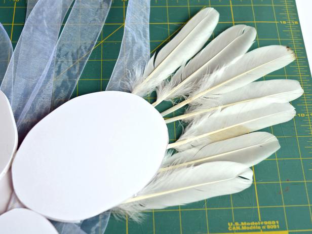 Step 4A is to turn the foam core base over so the side with ribbon straps is facing down. Arrange wide coquille goose feathers around the top edge of the large ovals to create the outside shape of wings.