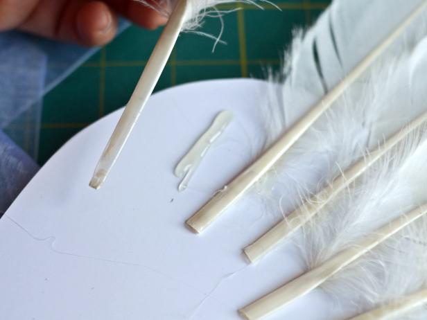 Step 5 in creating angel or fairy wings is to apply hot glue to a foam core board, a couple of inches below the area where feathers were inserted in Step 4.