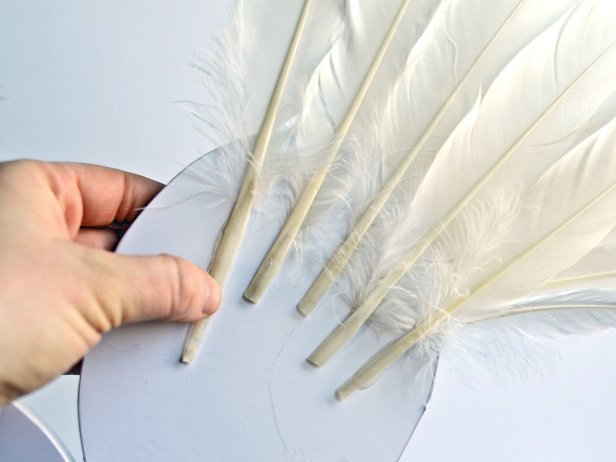 Step 5B in making feathered angel or fairy wings is to continue to layer feathers rows on the foam core board with hot glue until the wing shape is full.