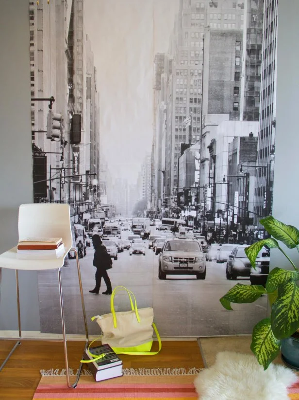 A large photograph of a busy city street creates a chic mural. A modern white barstool and colorful area rug accessorize the space.