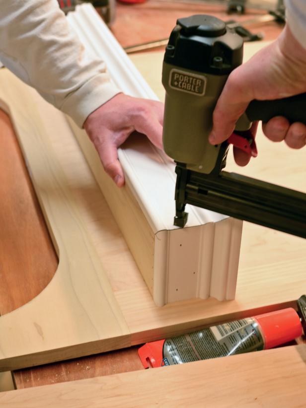 After dry-fitting the pieces together for a custom range hood project, the front and sides of the shelf can be nailed into place using a finishing nailer. Line the pieces up and hold them tightly during the attaching process.