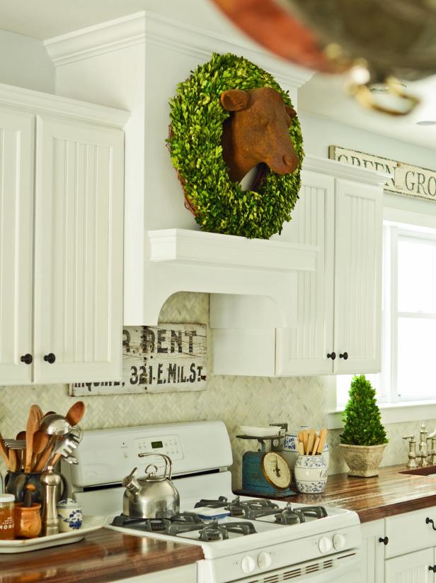 A custom range hood gives this country kitchen a high-end treatment. The marble herringbone backsplash and butcher block countertops add simple country style against the white cabinetry. An iron cow bust plays into the theme while a wreath around it's neck adds a splash of playful color.