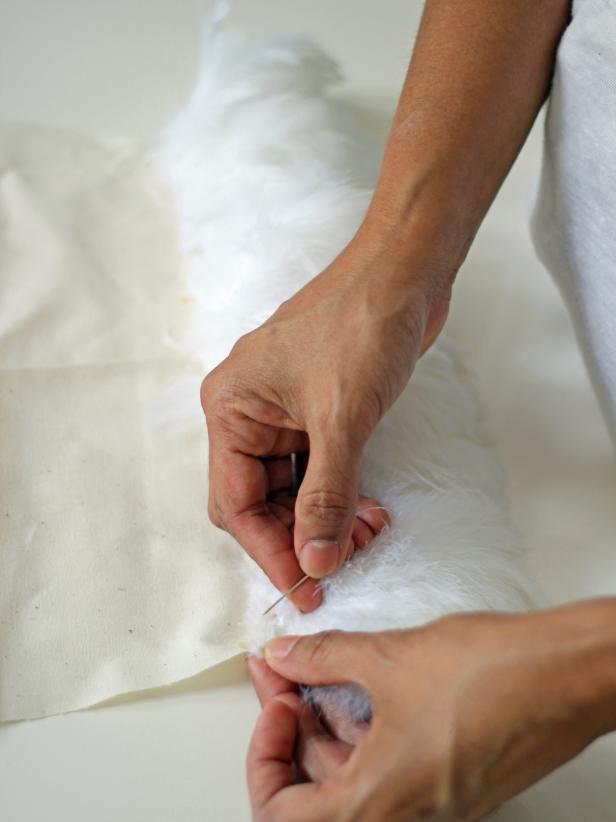 Step 4A in embellishing a vanity chair with feathers is to begin sewing strips of fabric onto the muslin fabric shape. Beginning at the top of the fabric, sew lengths of feathers across the fabric and continue rows from top to bottom.