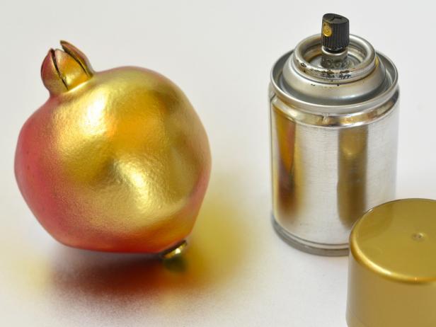 To make the pomegranate place holders, protect surface with newspaper or canvas, then coat each pomegranate with a light layer of gold spray paint.