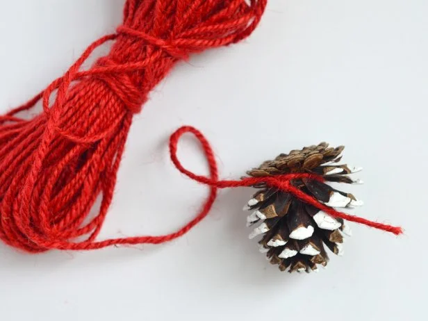 Wrap end of yarn around the bottom of a pinecone and knot.