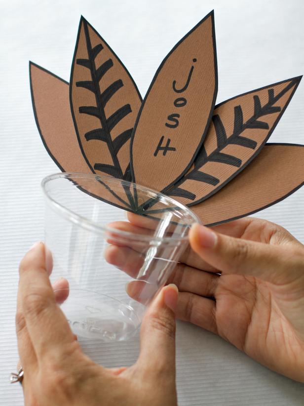 After centering the name card feather in the center of a plastic cup, hot glue four construction paper feathers on either side of the center feather to create the pheasant's tail feathers.