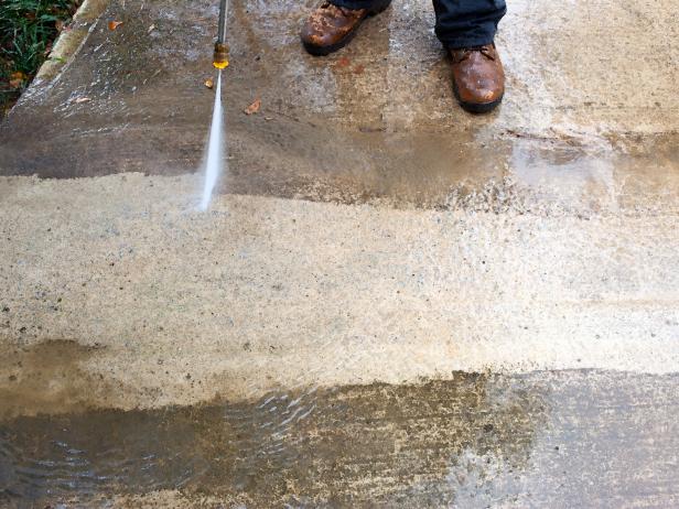 Pressure wash concrete by holding down spray handle, working your way back and forth from one side of concrete.