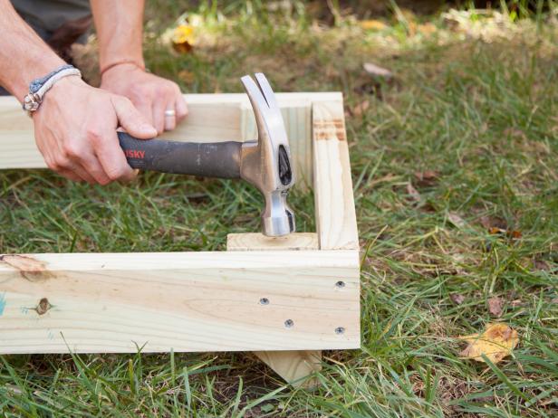 In this step, secure the sandbox frame to the ground by turning the frame over so that the spikes face downward, then hammer the spikes into the ground.