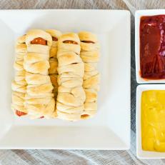 Tasty Halloween Mummy Dogs With Mustard and Ketchup Dipping Sauces