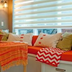 White Window Seat With Orange Cushion and Assorted Pillows
