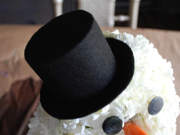 Use hot glue gun to secure wooden skewer inside a doll-sized top hat. Place hat on top of the 4-inch sphere until securely held in place with attached skewer.