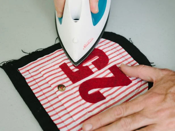 Trace numbers to felt using stencil as a guide. Next cut numbers out using fabric scissors. Once each number is cut out, attach to the front of a pocket using iron-on adhesive tape.