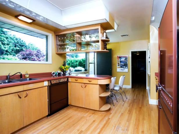 Wide view of a kitchen with hardwood floor, outdated countertops, and pale yellow walls.