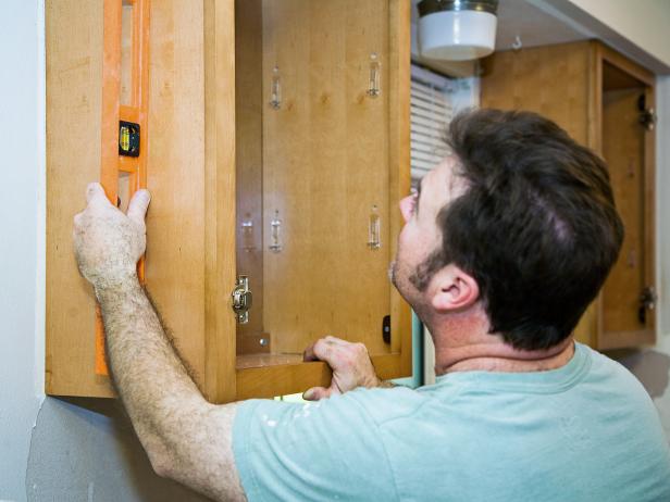 A man using a level to install kitchen cabinets.