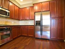 Wide view of oak kitchen cabinets, a wood floor, stainless kitchen appliances, and empty countertop.