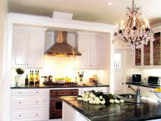 Rich green marble countertops and a stunning chandelier establish the elegant ambiance in this traditional kitchen. Stainless steel appliances stand out between understated white cabinets, completing the regal space.