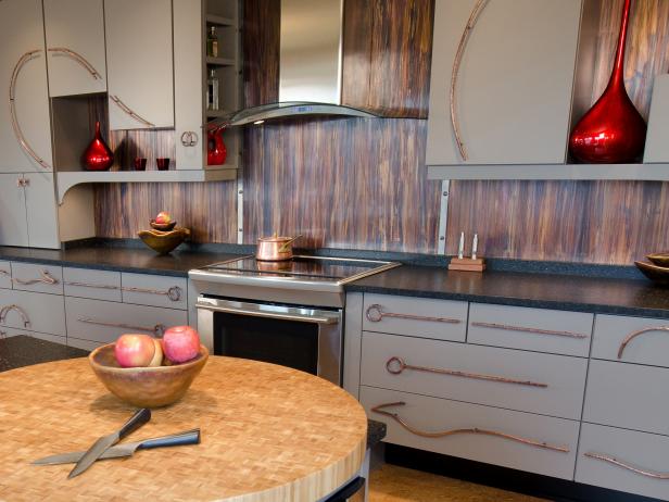Fanciful swirling metal pulls, fun red sculptural wall elements and a copper backsplash break free of the ordinary. Two sinks and two pullout trash containers eliminate prep conflicts.  Generous counter areas avoid bottlenecks for large prep, along with two appliance garages.