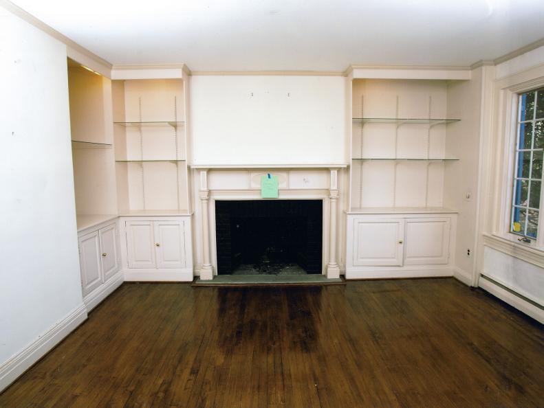 A before shot of this quaint living room shows the charming, off-center fireplace, which has built-in bookcases with glass shelves on either side.