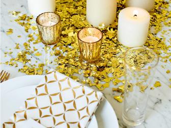 For this eye-catching centerpiece, large flecks of gold confetti are scattered in the middle of a dining table, and topped with large pillar candles and small votives.