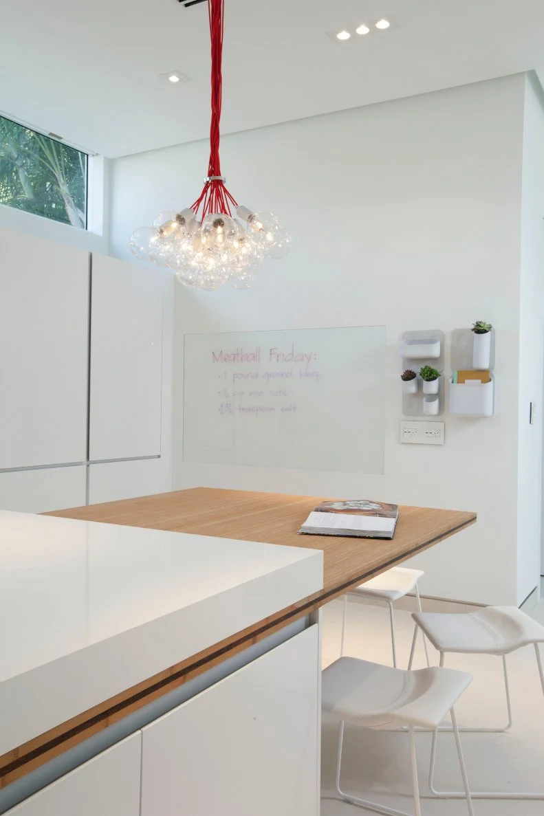 White, minimalist kitchen with bold, red-corded globe pendant cluster