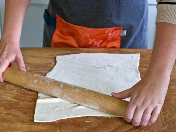 Thin out pastry dough with a rolling pin to make a cheese and herb wreath pastry for holiday guests.