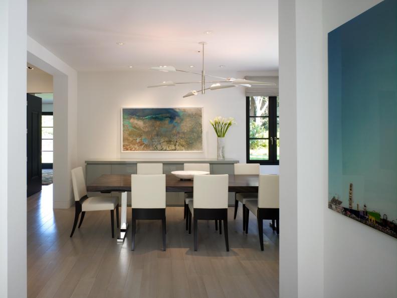 Hallway Opening to Modern White Dining Space With Long Wooden Table