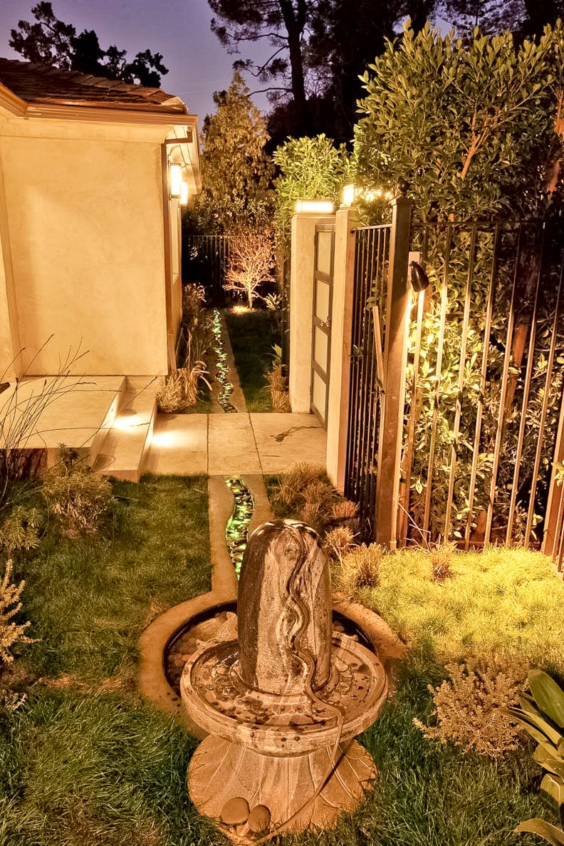 Stone Water Fountain in Backyard With Landscape Lighting