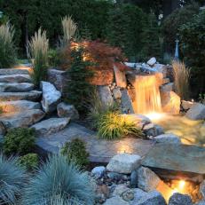 Beautifully Landscaped Yard With Boulder Staircase, Mixed Greenery and Lit Waterfall 