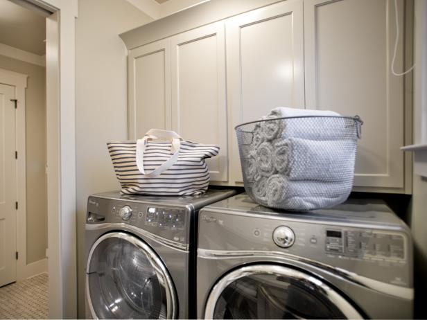 Neutral Laundry Room With White Cabinets and Front-Loading Appliances
