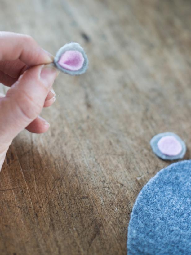 Center pink circle on top of larger light gray circle and stick pieces together. Repeat with second pink and gray pieces. Apply dab of glue to one corner of layered circles and pinch together to create an ear. Tip: Hold pinched shape in place with a clothespin while glue dries.