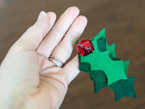 Pinch together 2-3 holly leaves for the cat toy of varying colors and shapes. Use green thread on an all-purpose sewing needle to secure leaves together at the top. Make sure stitch is strong, so leaves aren't easily pulled away during kitty's playtime. Once leaves are secure, use same thread to tack on two red bells, again, making sure they are secure.