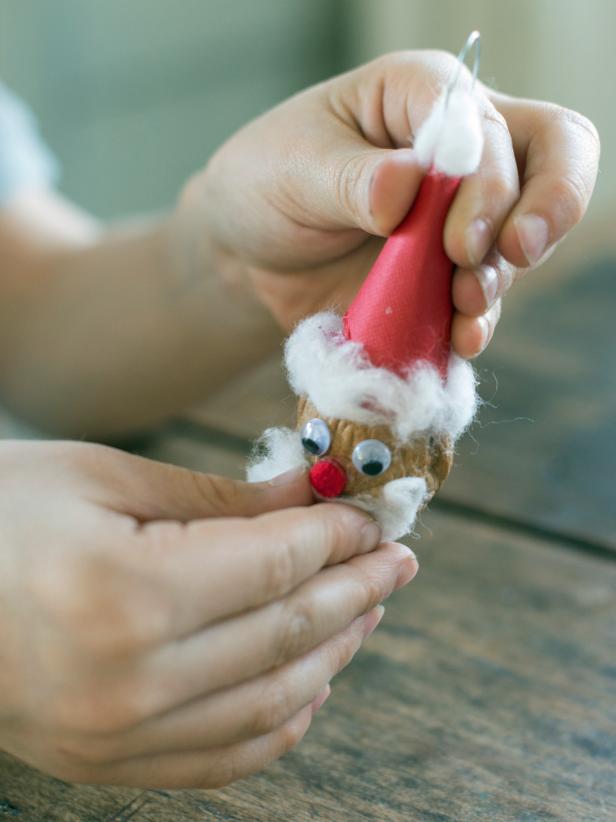 Glue craft eyes, red pompom nose and a cotton ball beard to the walnut to make Santa's face for the handmade ornament.